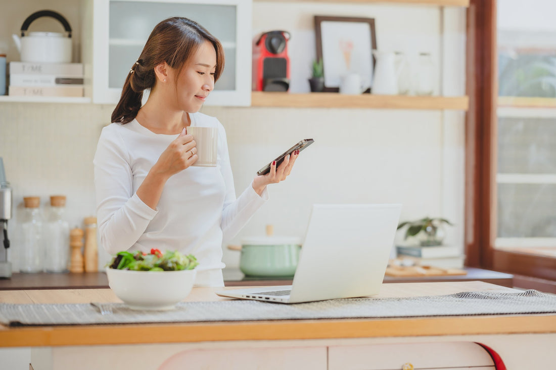 image of woman drinking coffee from a mug in a white kitchen with brown countertops