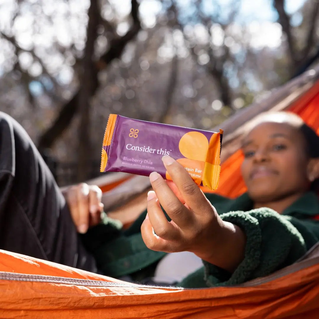 image of a woman in a hammock showing a blueberry chia protein bar